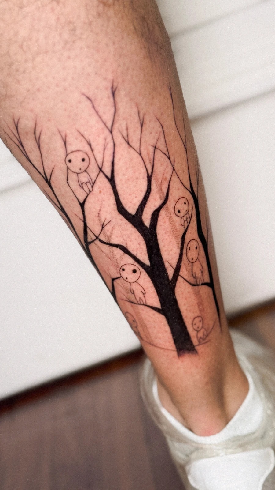 Tattoo of a leafless tree with small forest spirits (kodama, from Princess Mononoke) on the calf